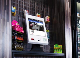 Die Selbstbedienungskasse Gen3 von 365 Retail Markets in einem Regal umgeben von Kassenvorsatz-/Impulsartikeln.